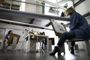 A view from below of multiple students in a drawing art class at Converse