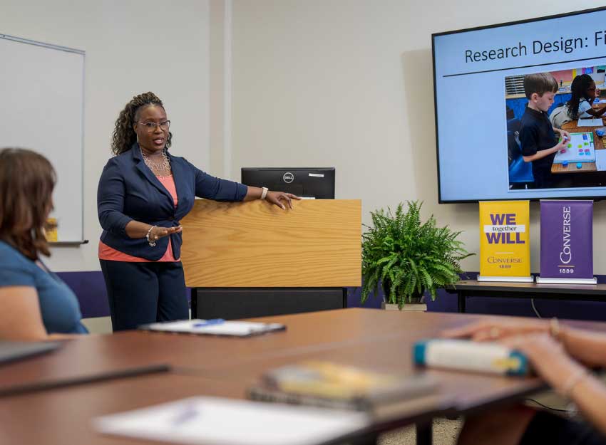 A teacher stands at a podium while presenting a power point