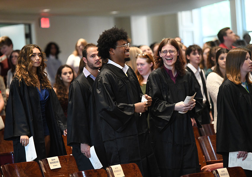 Students from the Converse Class of 2025 process smiling into Twichell Auditorium in their graduation gowns.