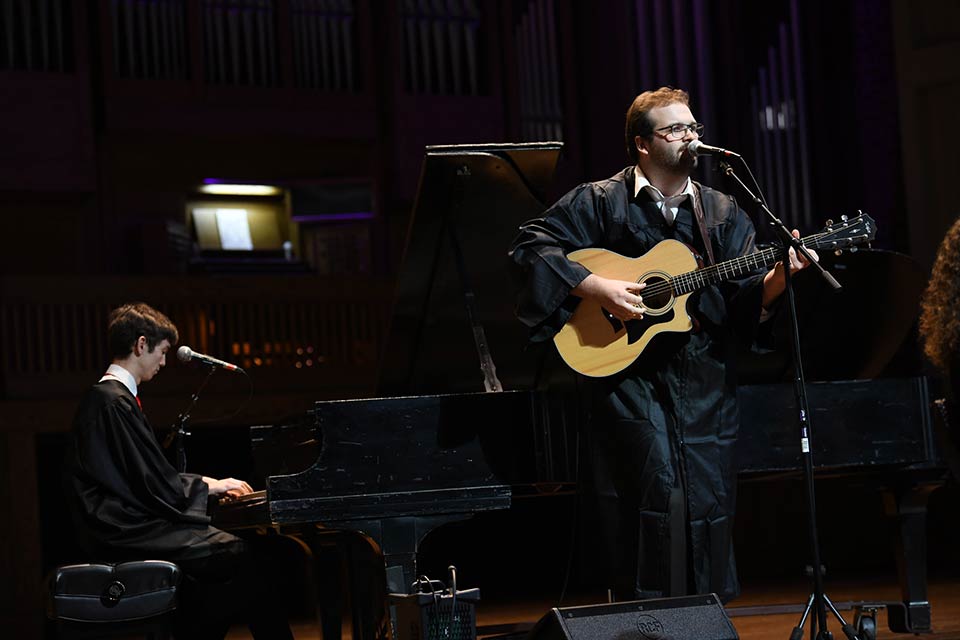 Aidan O’Donnell plays piano while Isaiah Caston sings and plays guitar onstage in Twichell Auditorium.