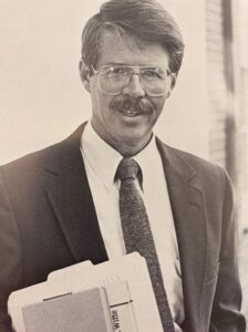 Dr. Mathews stands in a suit holding books.