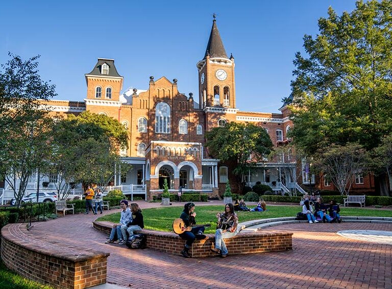 A group of students socialize on the front lawn of Converse campus on a warm, sunny day.