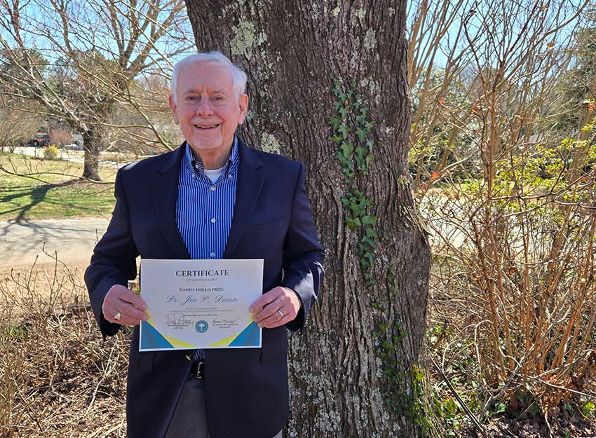 Dr. Joe Dunn stands smiling while holding his award.