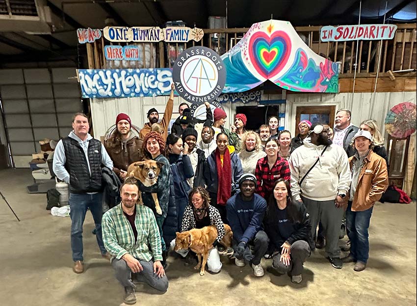 A group of volunteers stand in front of a sign that reads, "Grassroots Aid Partnership."