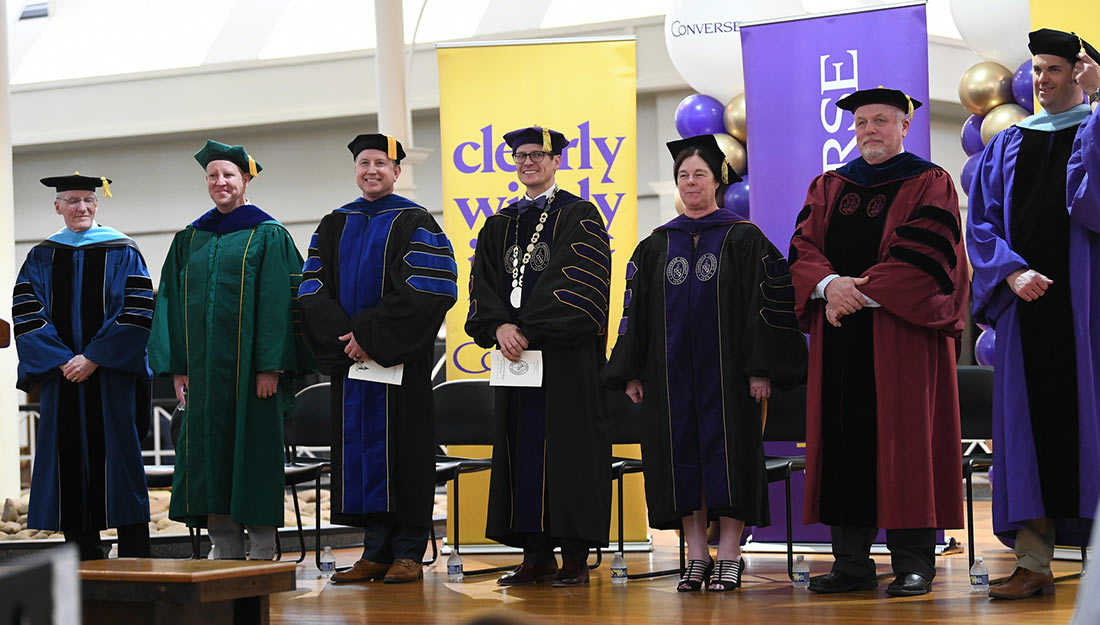 A group of Converse faculty stand on the stage at UCG during the doctoral ceremony.