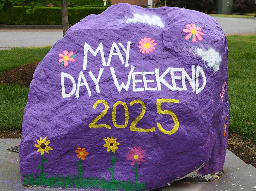 A large rock on the Converse campus with the words "May Day Weekend 2025" painted on it.