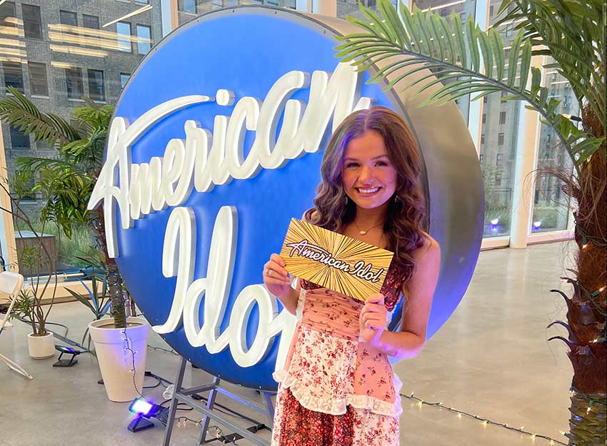 Jasmine Humphries stands in front of the American Idol sign holding her golden ticket.