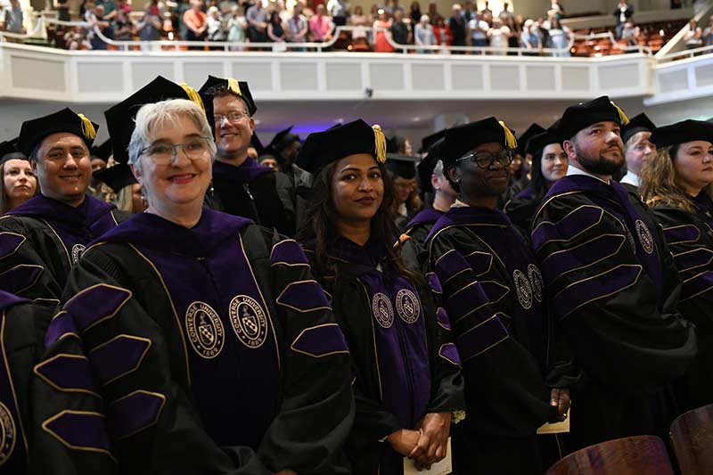 Graduate students smile as they stand in Converse's Twichell Auditorium for Commencement.