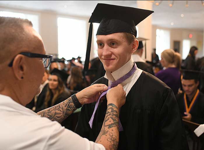 A staff member helps a student tie their tie at commencement.