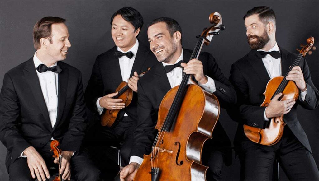 Four members of Miró Quartet pose with their instruments in black tie attire.