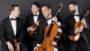 Four members of Miró Quartet pose with their instruments in black tie attire.