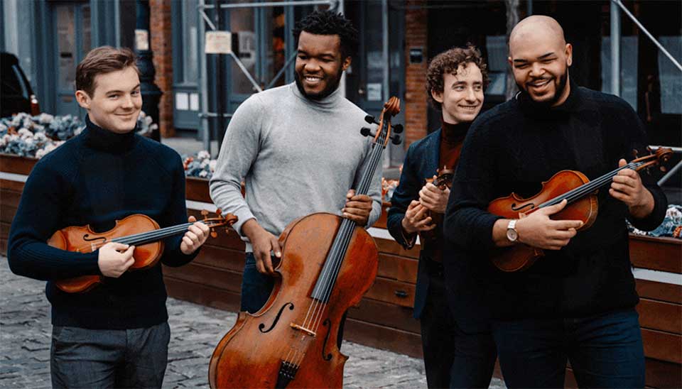 The members of the Isidore Quartet perform while walking down a cobblestone street.