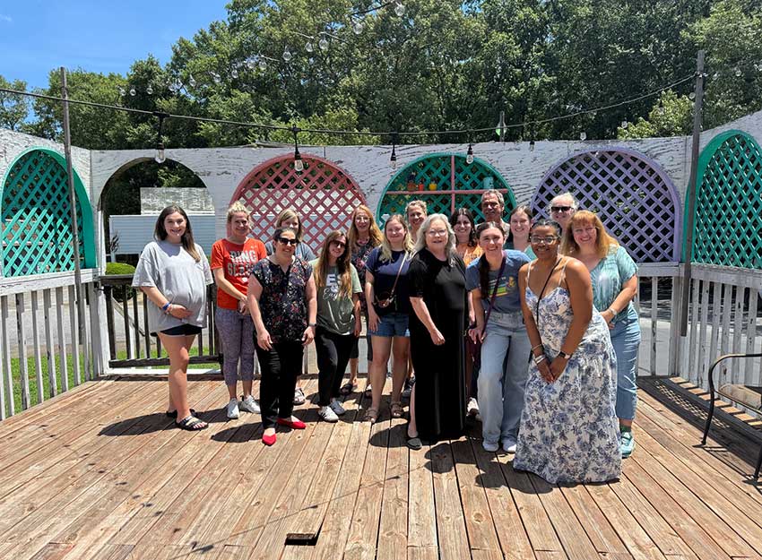 Graduate Converse students and faculty smile in a group photo at lunch during the summer intensive.
