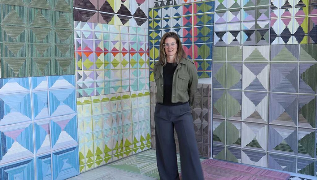 Artist Jean Alexander Frater stands in front of one of their paintings.