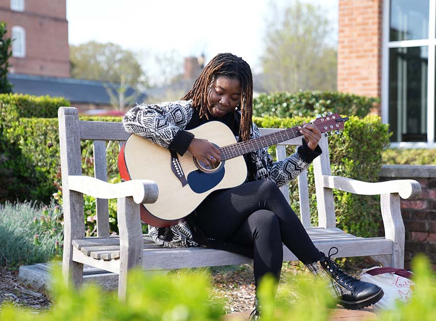 A Converse student plays the guitar outdoors.
