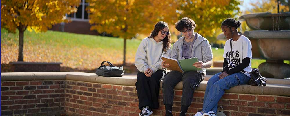 Three Converse students read by a campus fountain