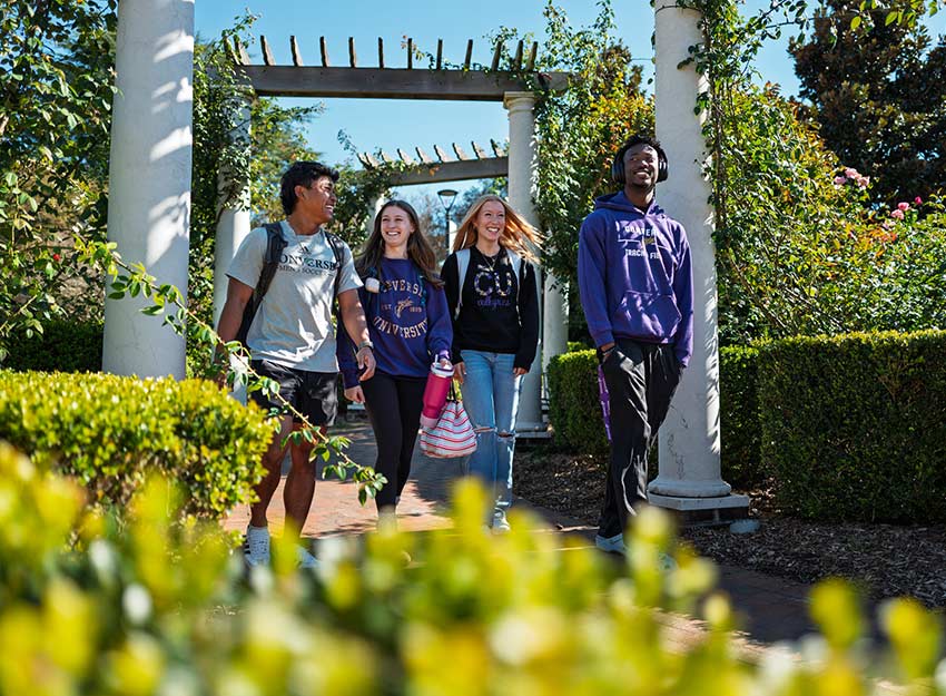A group of students walk under awnings on a sunny day on campus.