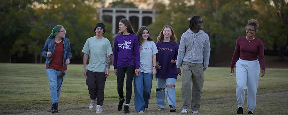 A large group of Converse students walk across the Quad on campus at sunset.