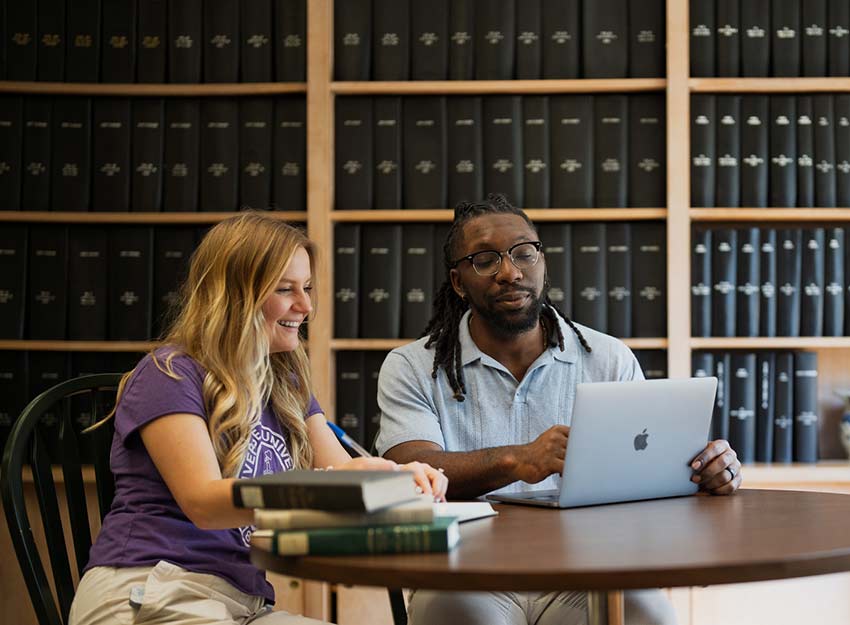 Two students study in front of a massive bookshelf.