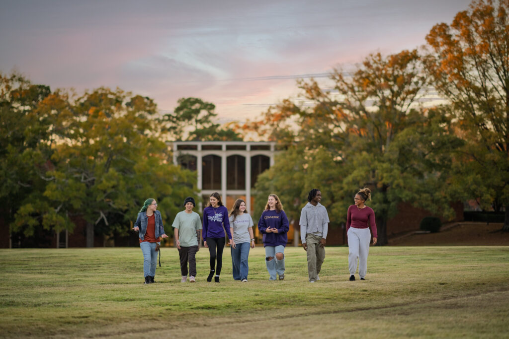 A group of Converse students walk across the campus quad at sunset.