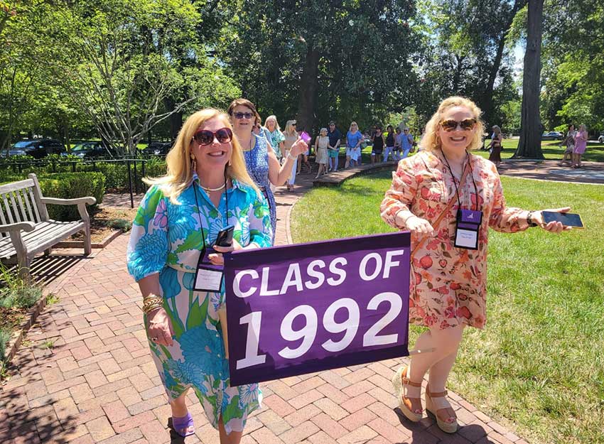 Rose walks with a friend at Converse reunion carrying a sign that says 'Class of 1992'.
