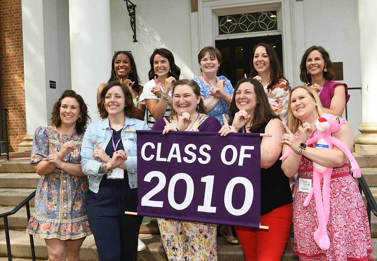 A group of alumni smile and hold a sign with their class year at a reunion event.