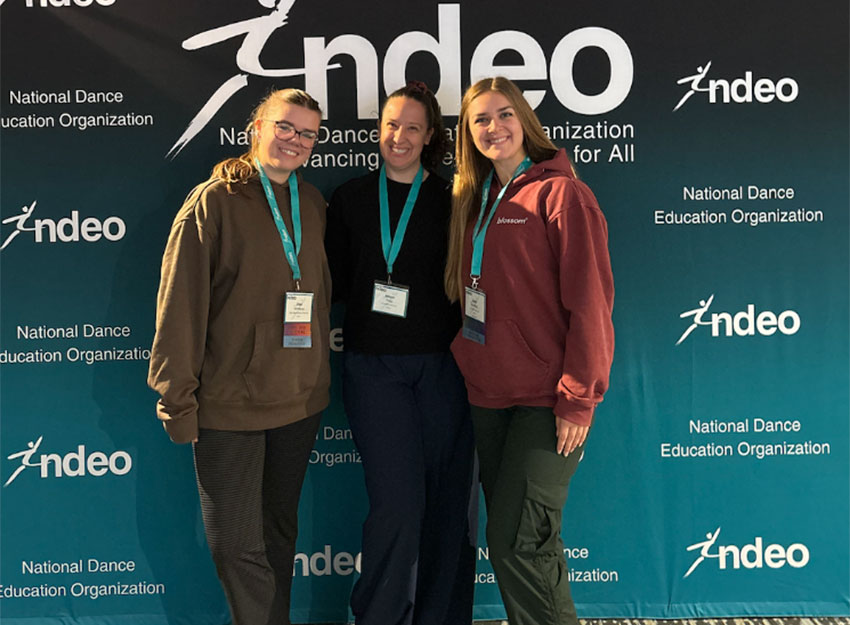A group of Converse students pose in front of a sign at the NDEO conference in Detroit.