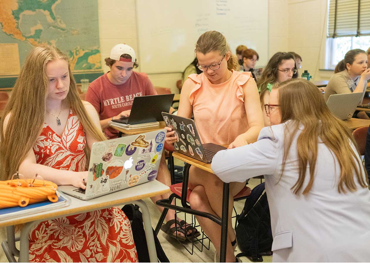 A Converse faculty member works with students in a classroom setting.