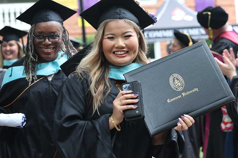 A new Graduate student holds their diploma while beaming.
