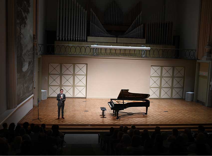 A piano on a mostly empty stage with dramatic lighting.