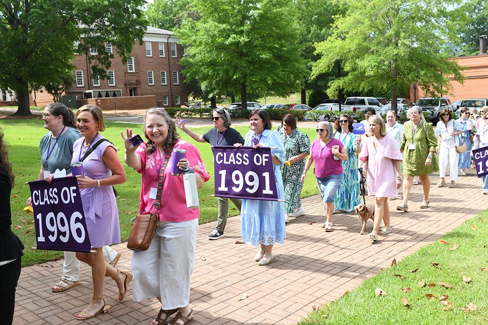 Alumni from a variety of classes process at Converse reunion holding the sign for their class year