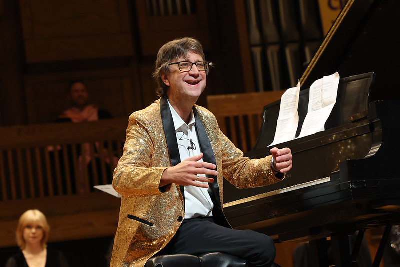Steven Graff smiles broadly while sitting at a piano on stage at convocation 2026.